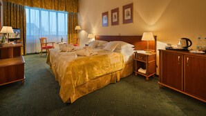 A hotel room with a large bed, bedside tables, a desk, a chair, and a view of the city through the window. - EA Hotel Rokoko (Prague)