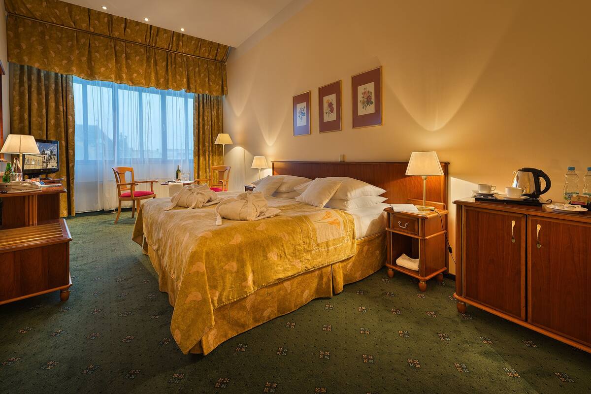 Habitación de hotel con una cama grande, mesitas de noche, un escritorio, una silla y vistas a la ciudad desde la ventana.