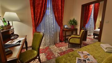 A hotel room with a bed, two chairs, a desk with a lamp, a laptop, and a small table with a plant.