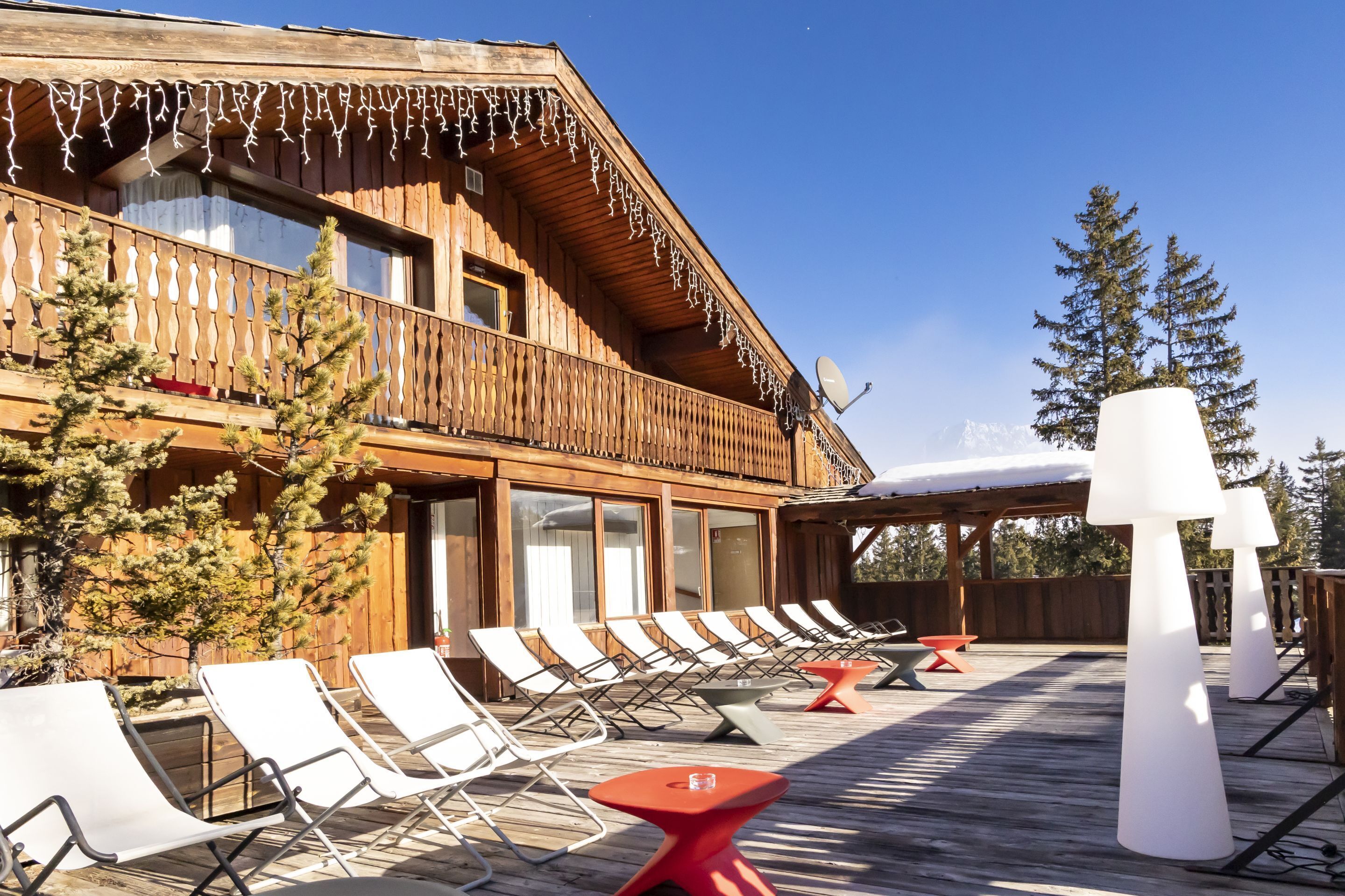 A wooden building with a balcony, lounge chairs, and tables arranged on a deck.