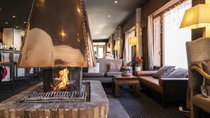 A cozy lounge area with a fireplace, comfortable seating, and a bar in the background. - Odalys Hotel New Solarium (Courchevel)