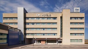 A modern hotel building with multiple floors, a prominent sign for NH Hotels, and a parking lot in front. - NH Alcorcón (Alcorcon)