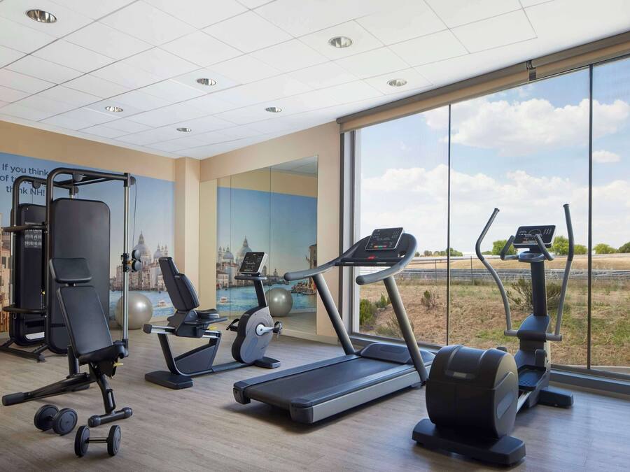 Un gimnasio con equipo cardiovascular, máquinas de pesas y un amplio ventanal con vistas al exterior.