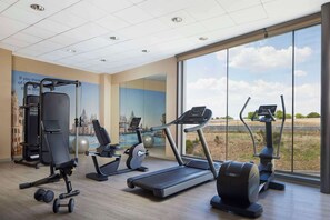 A gym with cardio equipment, weight machines, and a large window with a view of the outdoors. - NH Alcorcón (Alcorcon)