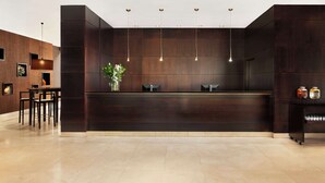 A reception area with a dark wood reception desk, three pendant lights, a vase with flowers, and a small side table with jars. - NH Alcorcón (Alcorcon)