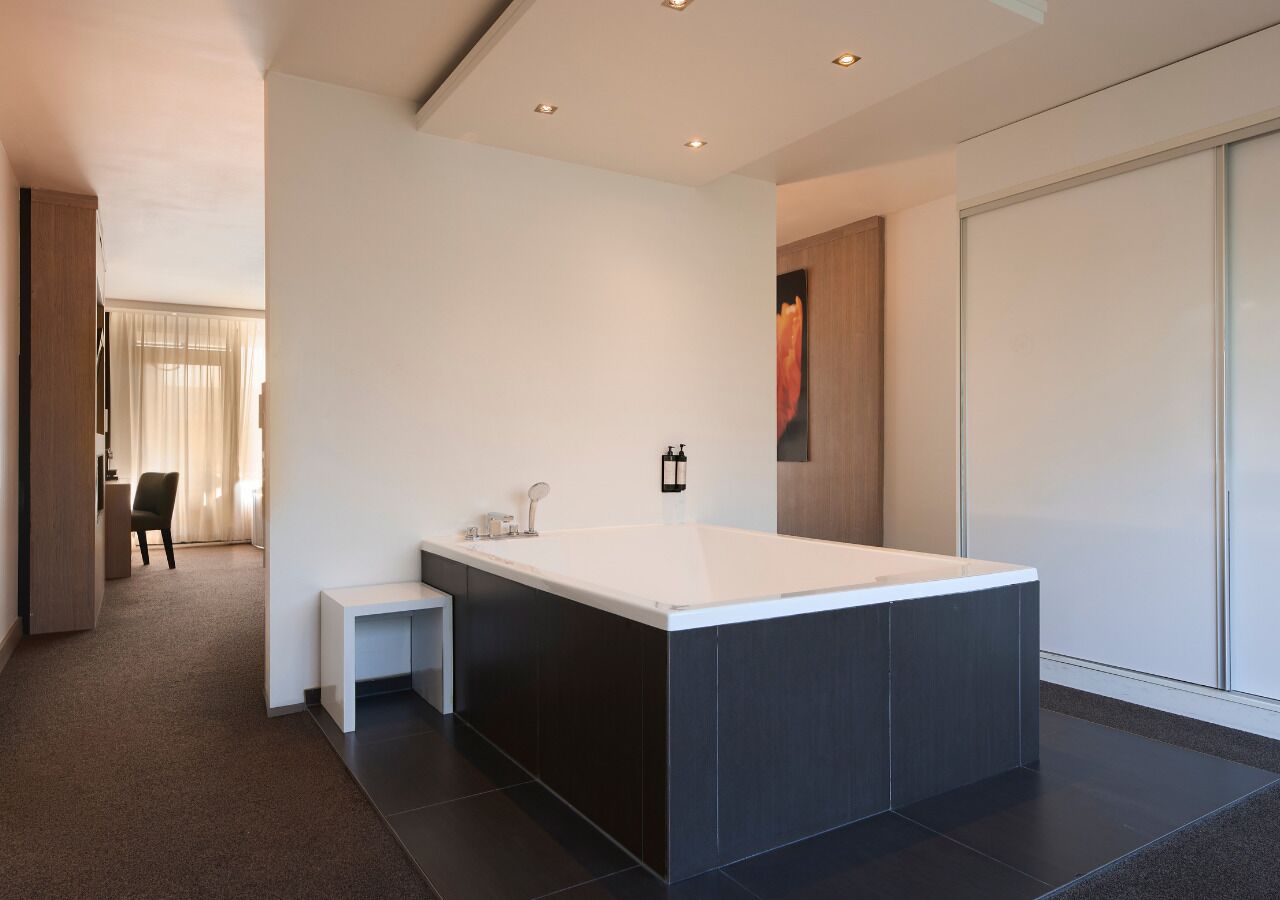 Un baño moderno con una bañera grande, un banco pequeño y un aplique de pared.
