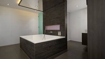 A modern bathroom with a large bathtub, dark tiled walls, and a mirrored ceiling.