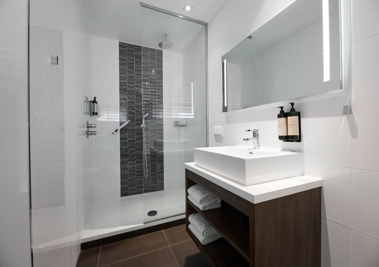 Une salle de bain moderne avec une douche à parois de verre, un lavabo blanc et un miroir au-dessus.