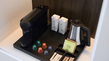 Een koffiehoek met koffiezetapparaat, melkpakken, een theepot en diverse koffiecups.