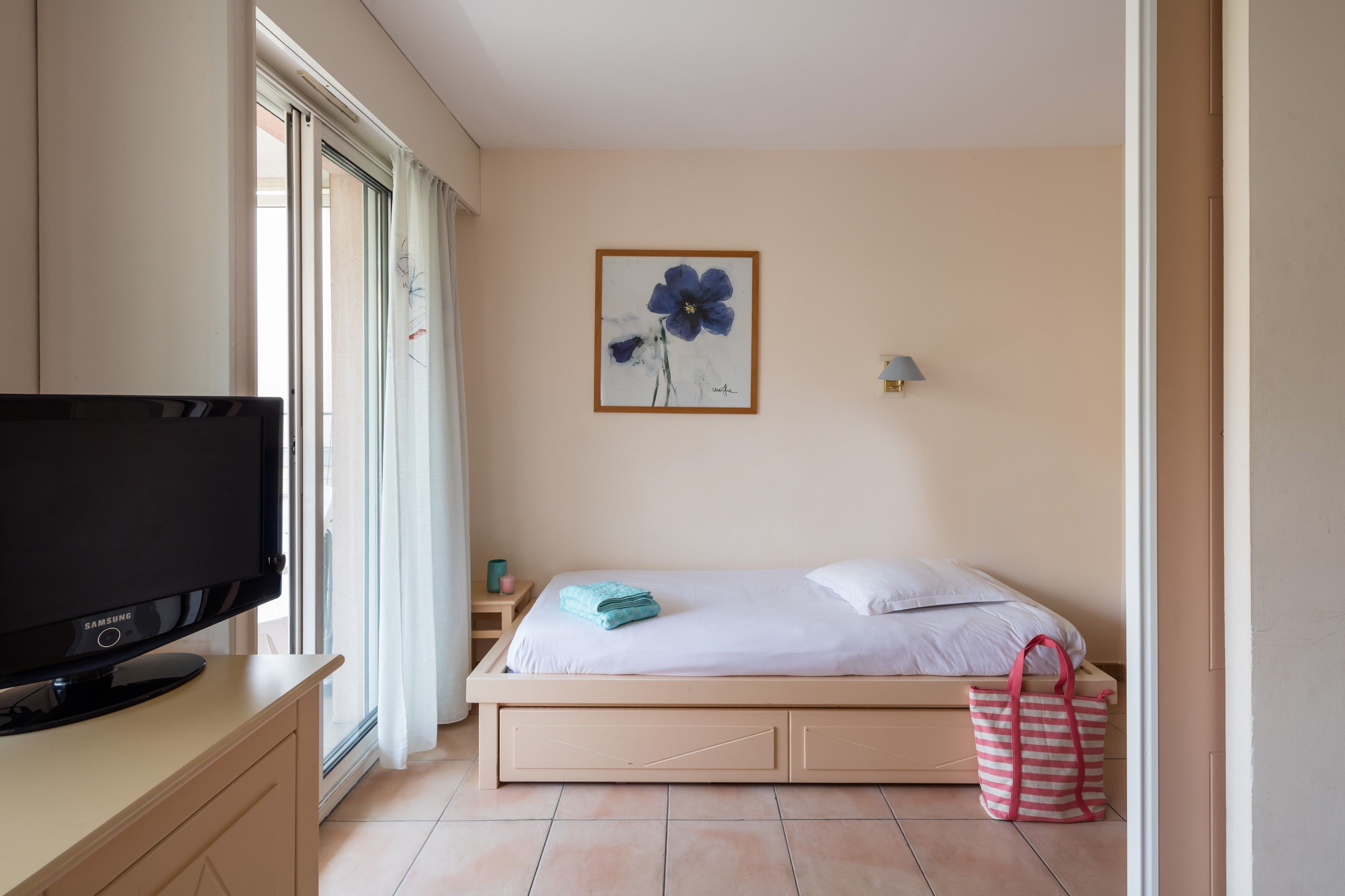 A bedroom with a bed, a TV, a painting, and a window.
