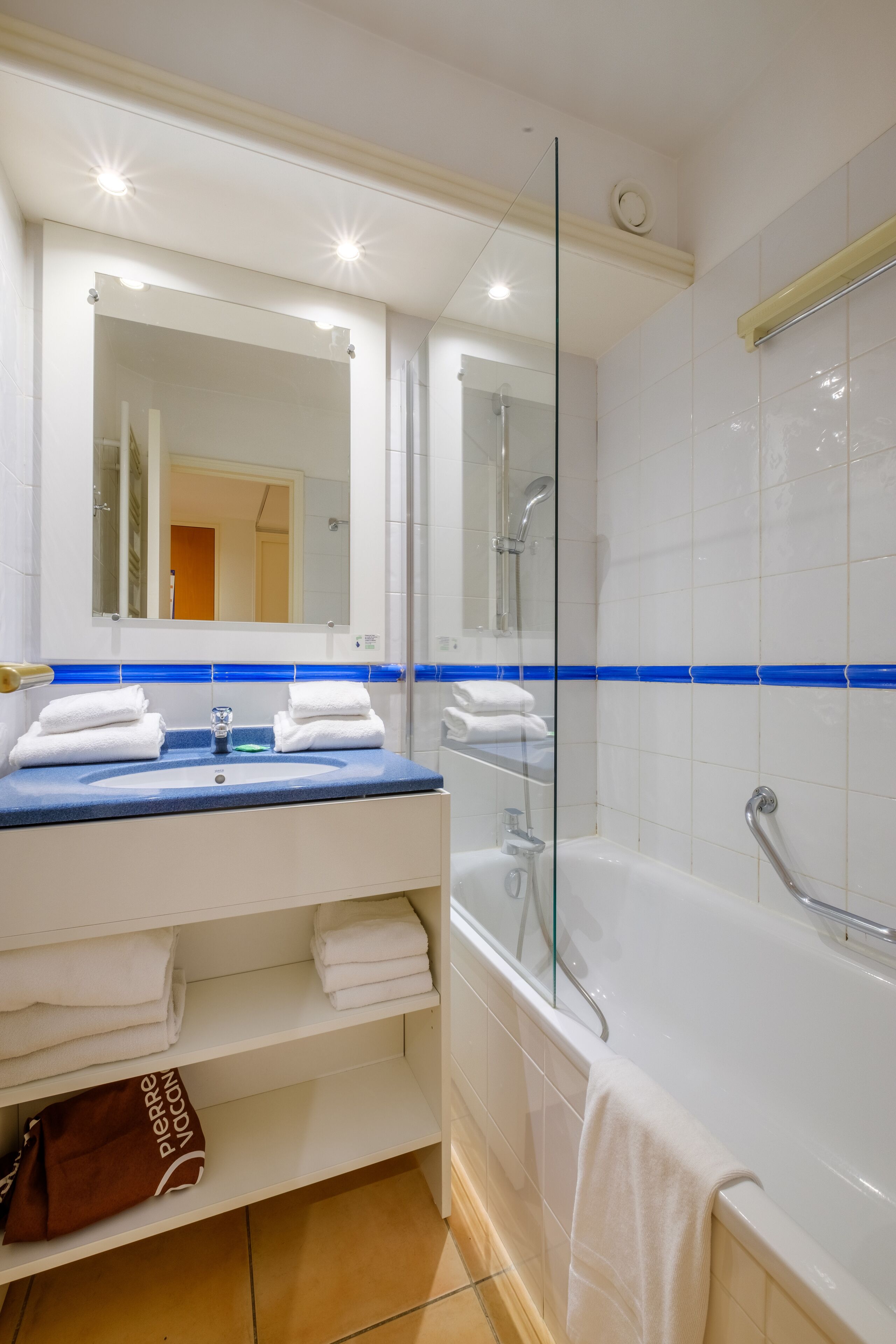 Une salle de bain moderne avec une douche à parois de verre, une baignoire blanche et un meuble-lavabo doté d’un plan de travail bleu.