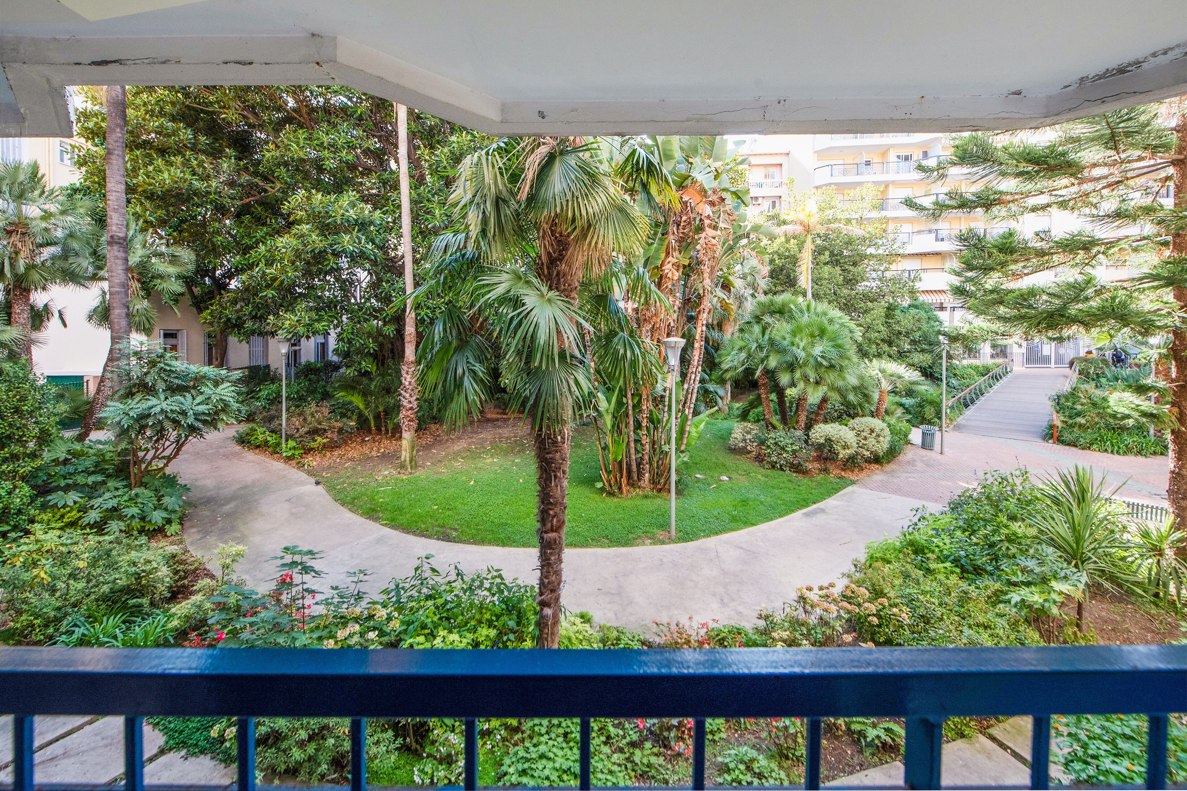 Ein Balkon mit Blick auf einen üppigen Garten, einen Pfad und ein Gebäude im Hintergrund.
