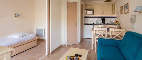 A compact hotel room with a bed, a small table, a sofa, a kitchenette, and a bathroom.