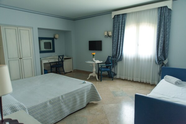 A hotel room with a bed, a desk with a chair, a small table with a vase, and a television on the wall. - Relais Antiche Saline (Paceco)