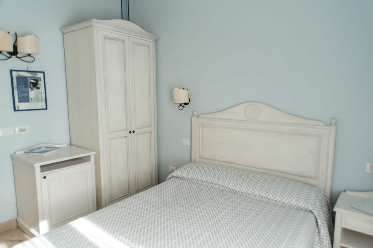 A bedroom with a bed, a wardrobe, a nightstand, and a wall-mounted lamp.