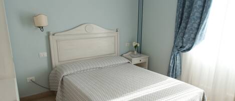 A bedroom with a bed, bedside table, lamp, and curtains.