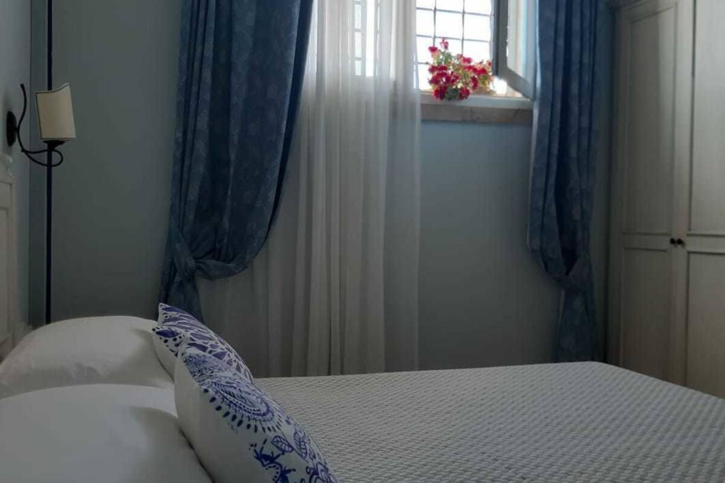 Un dormitorio con cama, ventana con cortinas y lámpara en la pared.