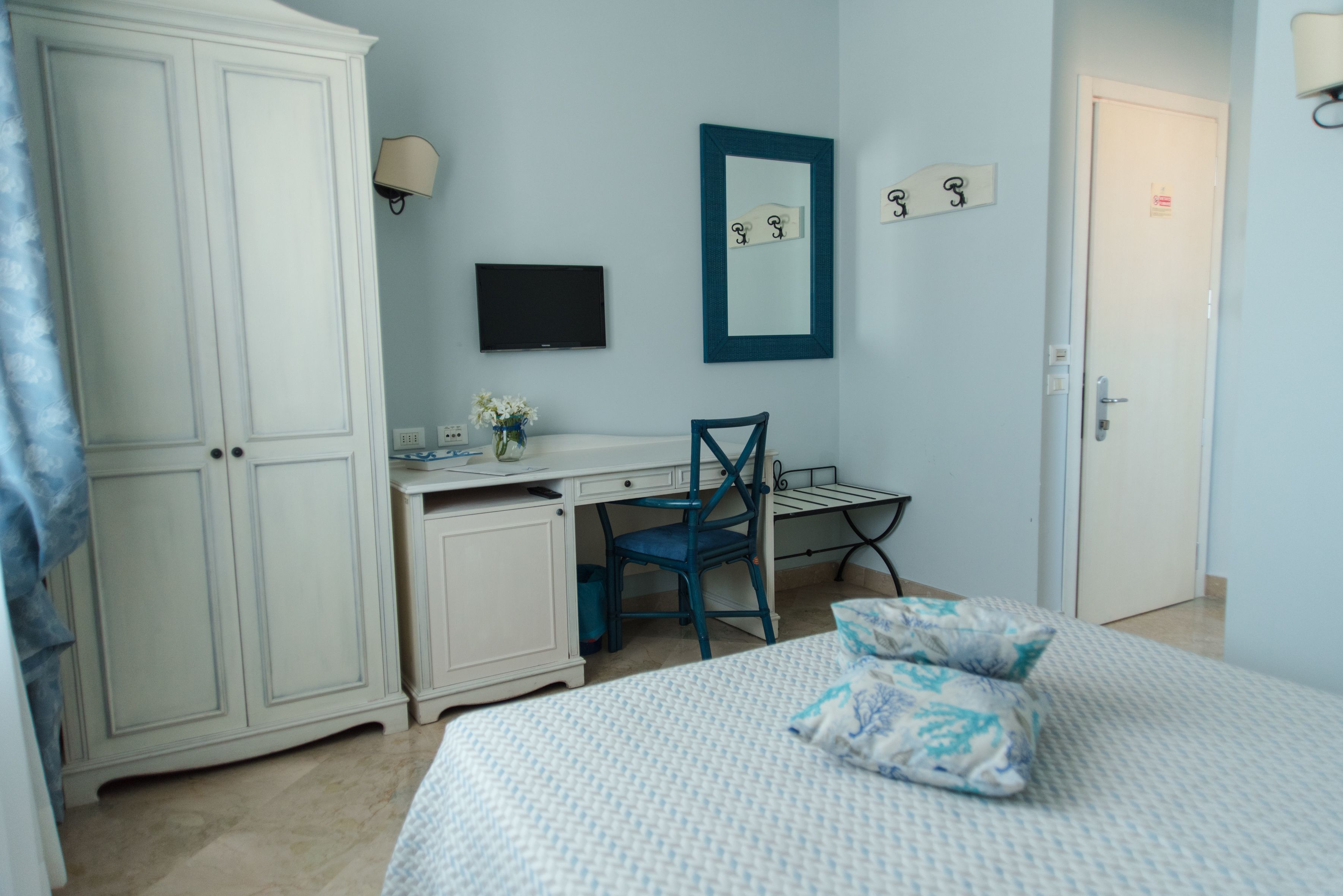 A bedroom with a bed, a desk, a chair, a wardrobe, a television, and a mirror.