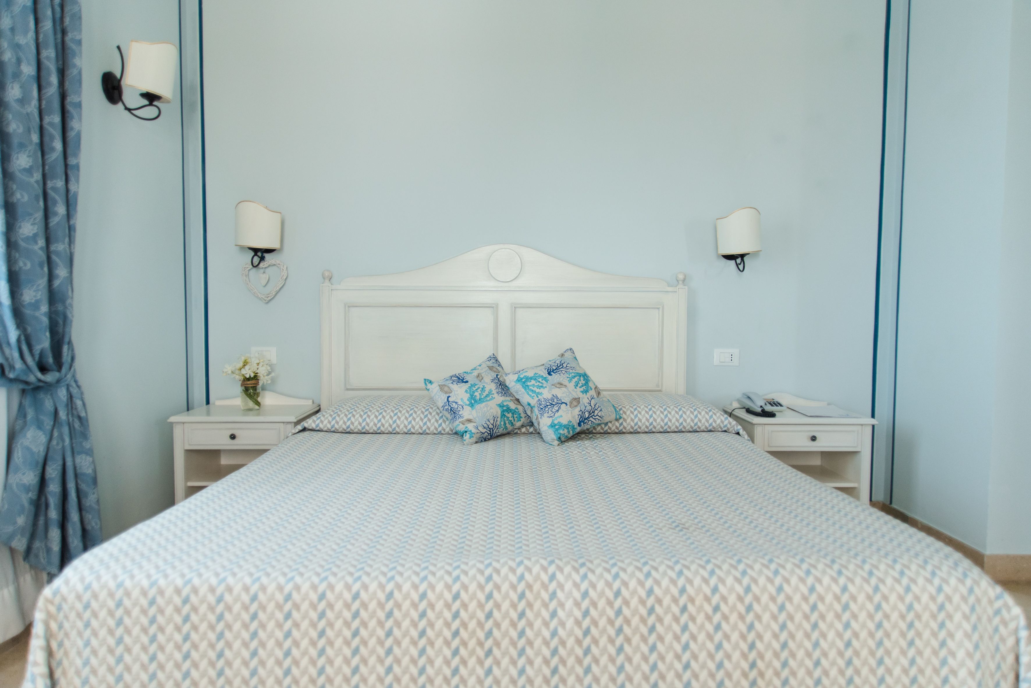 Un dormitorio con una cama, dos mesitas de noche, una lámpara y una luz empotrada en la pared.