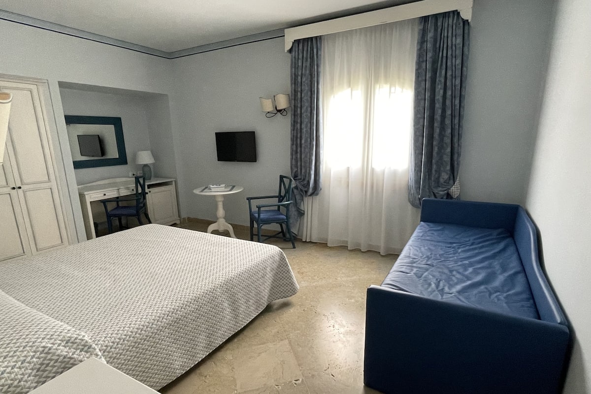 A hotel room with two beds, a desk, a chair, a TV, and a window with curtains.
