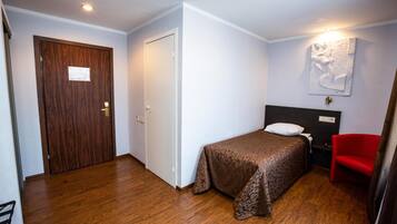 Una habitación pequeña y ordenada con una cama, una silla roja y una puerta de madera.