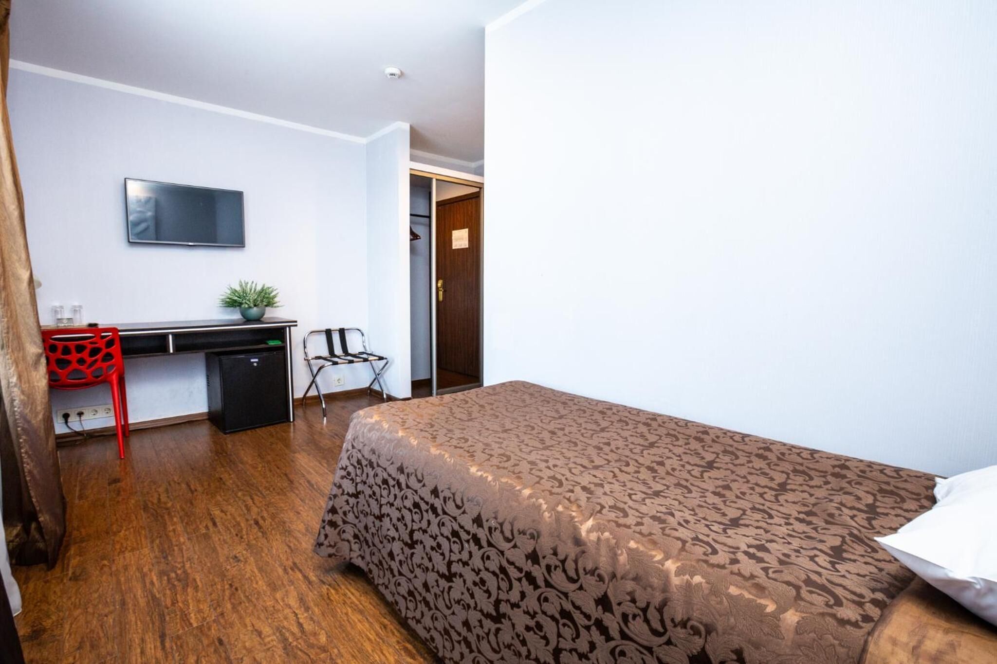 Hotellihuone, jossa on sänky, työpöytä, televisio ja pieni kasvi.