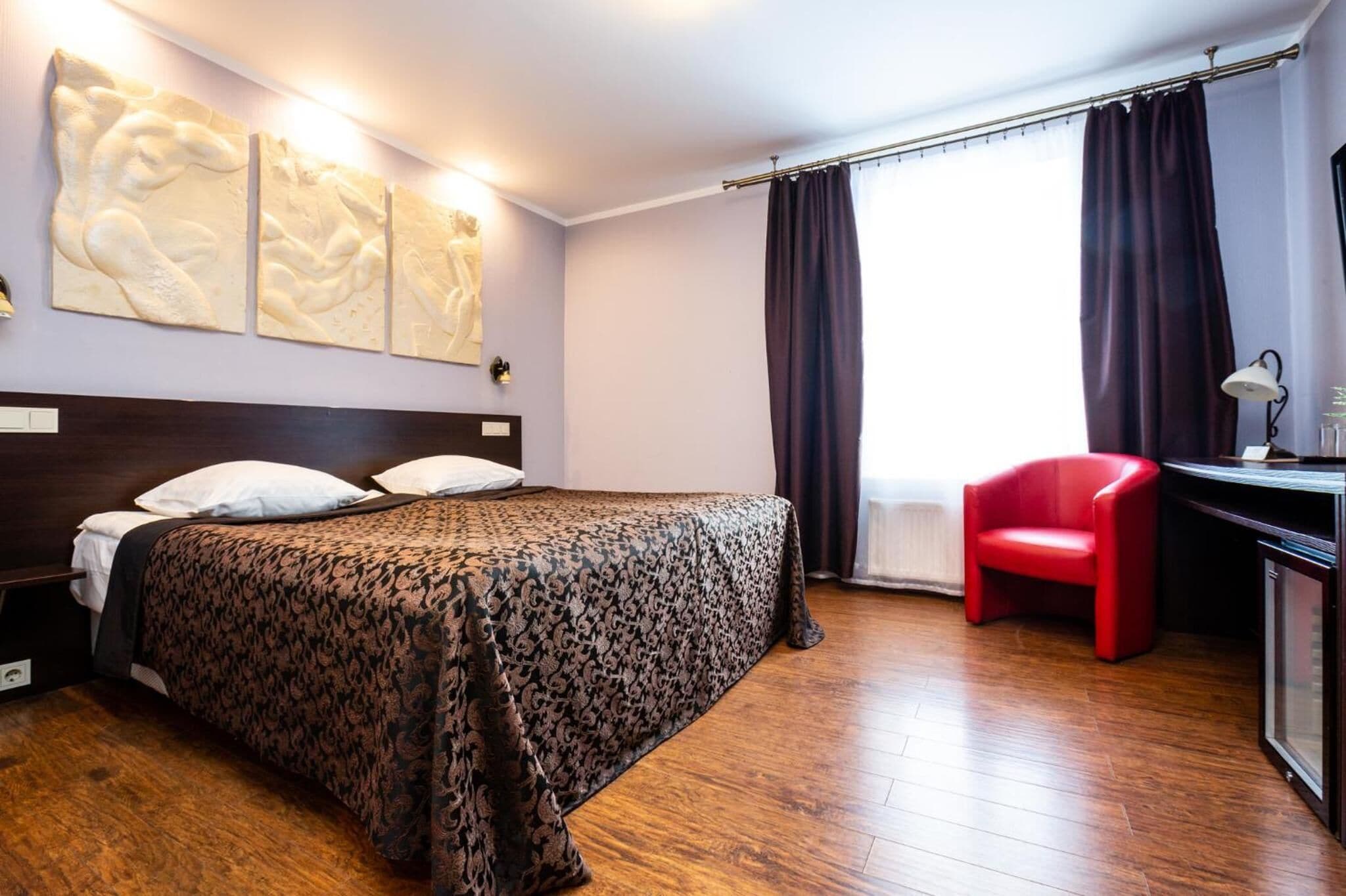 Hotellihuone, jossa on suuri sänky, työpöytä tuolilla sekä ikkuna, jossa on verhot.
