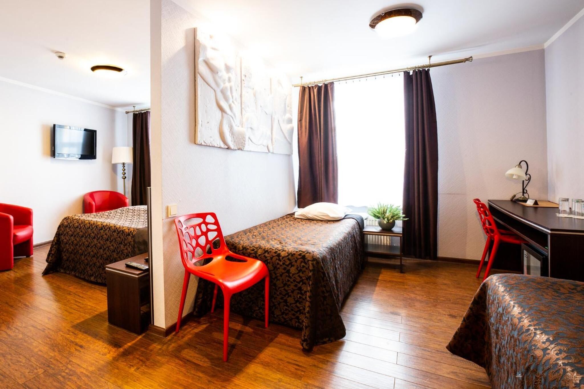 Una habitación de hotel con dos camas, un escritorio, una silla, un televisor y una ventana con cortinas.