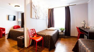 Una habitación de hotel con dos camas, un escritorio, una silla, un televisor y una ventana con cortinas.