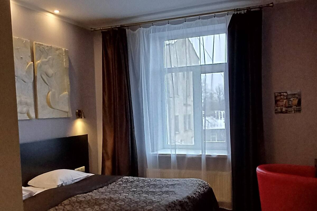 Ein Hotelzimmer mit einem großen Bett, einem roten Sessel und einem Fenster mit Vorhängen.