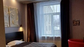 A hotel room with a large bed, a red chair, and a window with curtains.