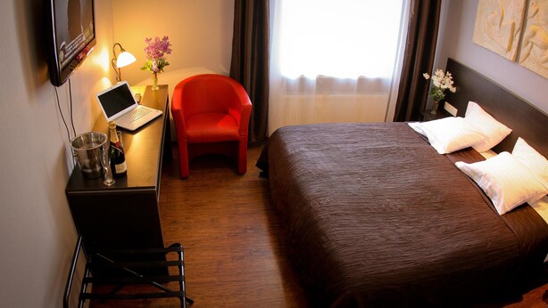 Habitación de hotel con cama, escritorio con computadora portátil, silla, televisión y ventana con cortinas.