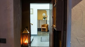 Un pasillo con piso de cuadros, un lámpara colgante y una puerta que da a una habitación con una silla y una planta.