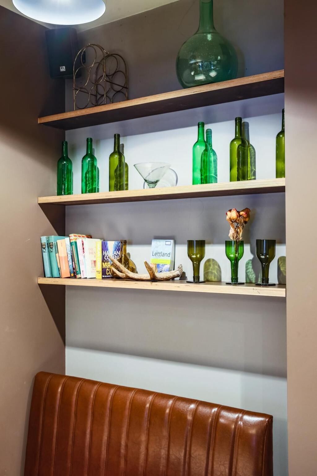 A bookshelf with green glass bottles, books, and decorative items.