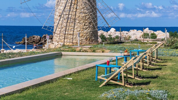 Un molino con piscina y sillas de descanso en un entorno soleado al aire libre.