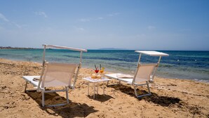 Dos sillas de playa con sombrillas, una mesita con bebidas y una vista despejada del mar.