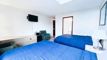 Quarto de hotel com duas camas, uma escrivaninha, uma cadeira, uma televisão e uma porta.