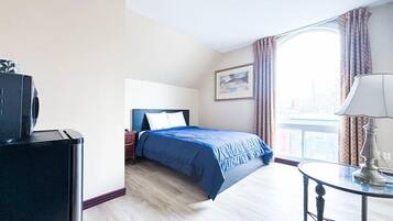 Una habitación de hotel con cama, escritorio, lámpara y ventana con cortinas.