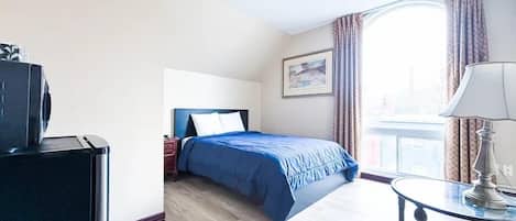 A hotel room with a bed, a desk, a lamp, and a window with curtains.