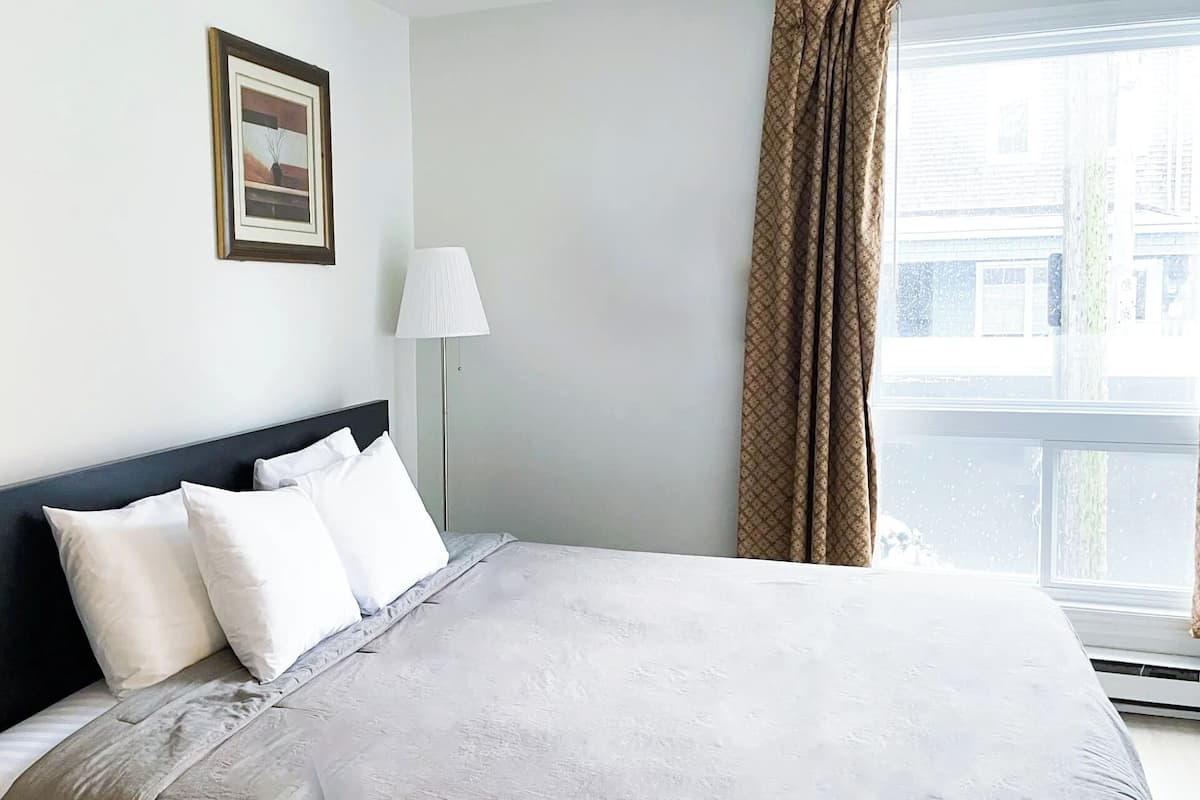 A hotel room with a bed, a nightstand, a lamp, and a window with curtains.