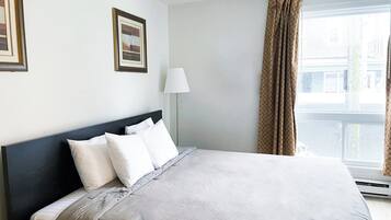 Una habitación de hotel con cama, mesita de noche, lámpara y ventana con cortinas.