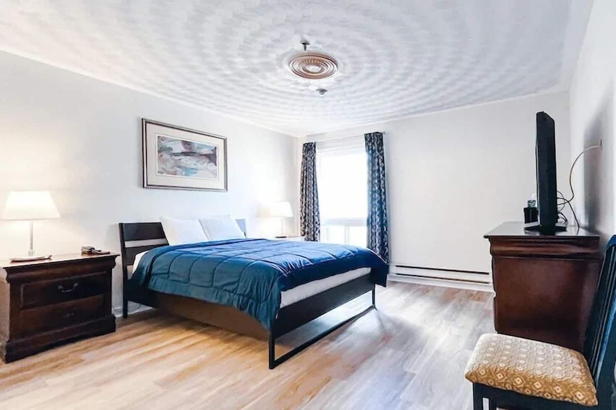 A hotel room with a bed, a desk, a chair, a TV, a painting, and a window with curtains.