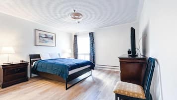 Una camera d'albergo con un letto, una scrivania, una sedia, una televisione, un quadro e una finestra con tende.
