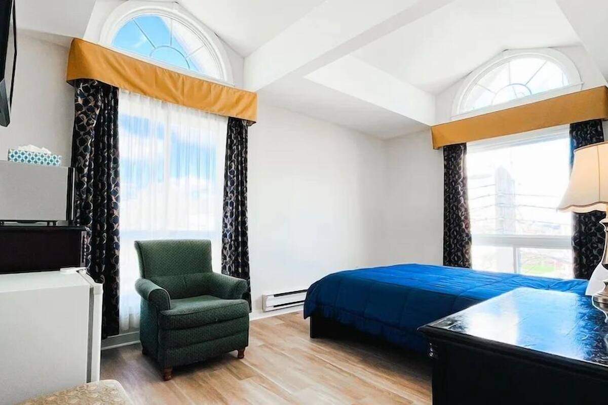 A hotel room with a bed, a chair, a desk, and a lamp.