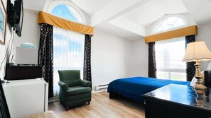 A hotel room with a bed, a chair, a desk, and a lamp.