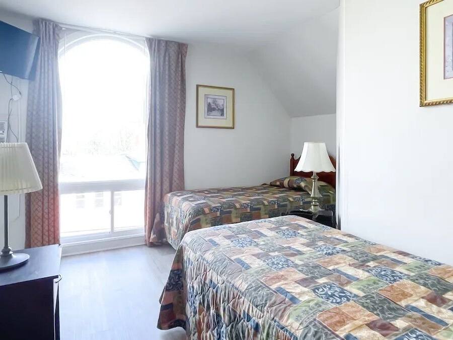 A hotel room with two beds, a desk, a lamp, a window with curtains, and a framed picture on the wall.