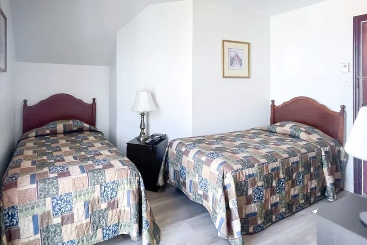 A hotel room with two beds, each with a patterned bedspread, a bedside table with a lamp, and a framed picture on the wall.