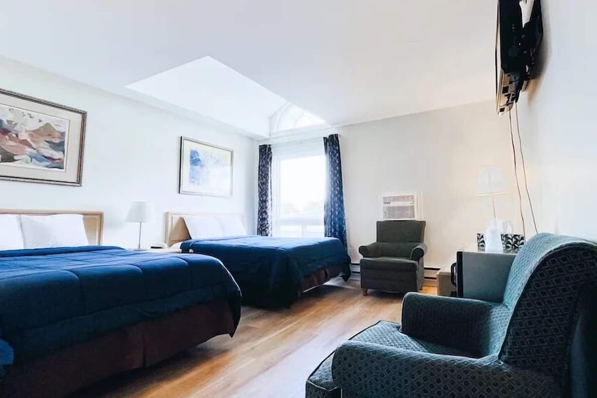 A hotel room with two beds, a desk, a chair, and a TV.