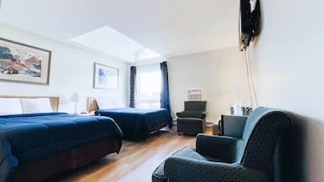 A hotel room with two beds, a desk, a chair, and a TV.