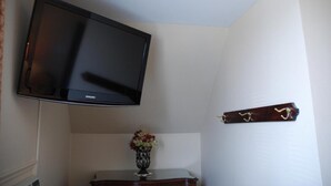 A room with a mounted television on the wall, a small table with a vase of flowers, and a coat rack with a single item.